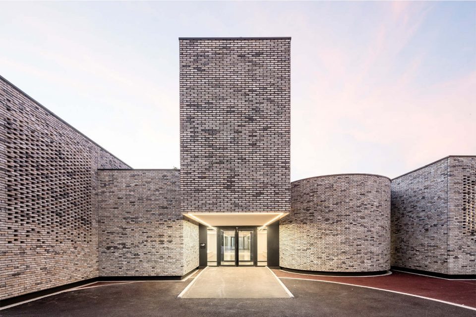 La façade en brique claires effet moucharabbieh de l'école de musique d’Élancourt, vue au coucher du soleil avec l'illumination de la porte.