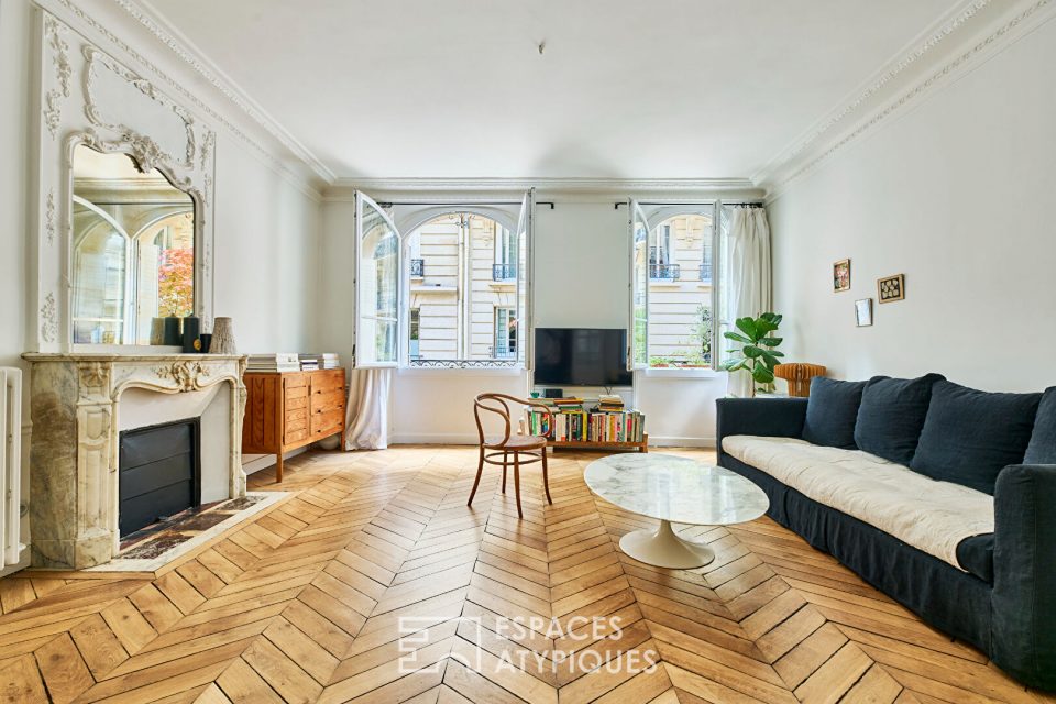 Salon d'un appartement haussmannien, cheminée en marbre, parquet, moulures et grandes fenêtres.