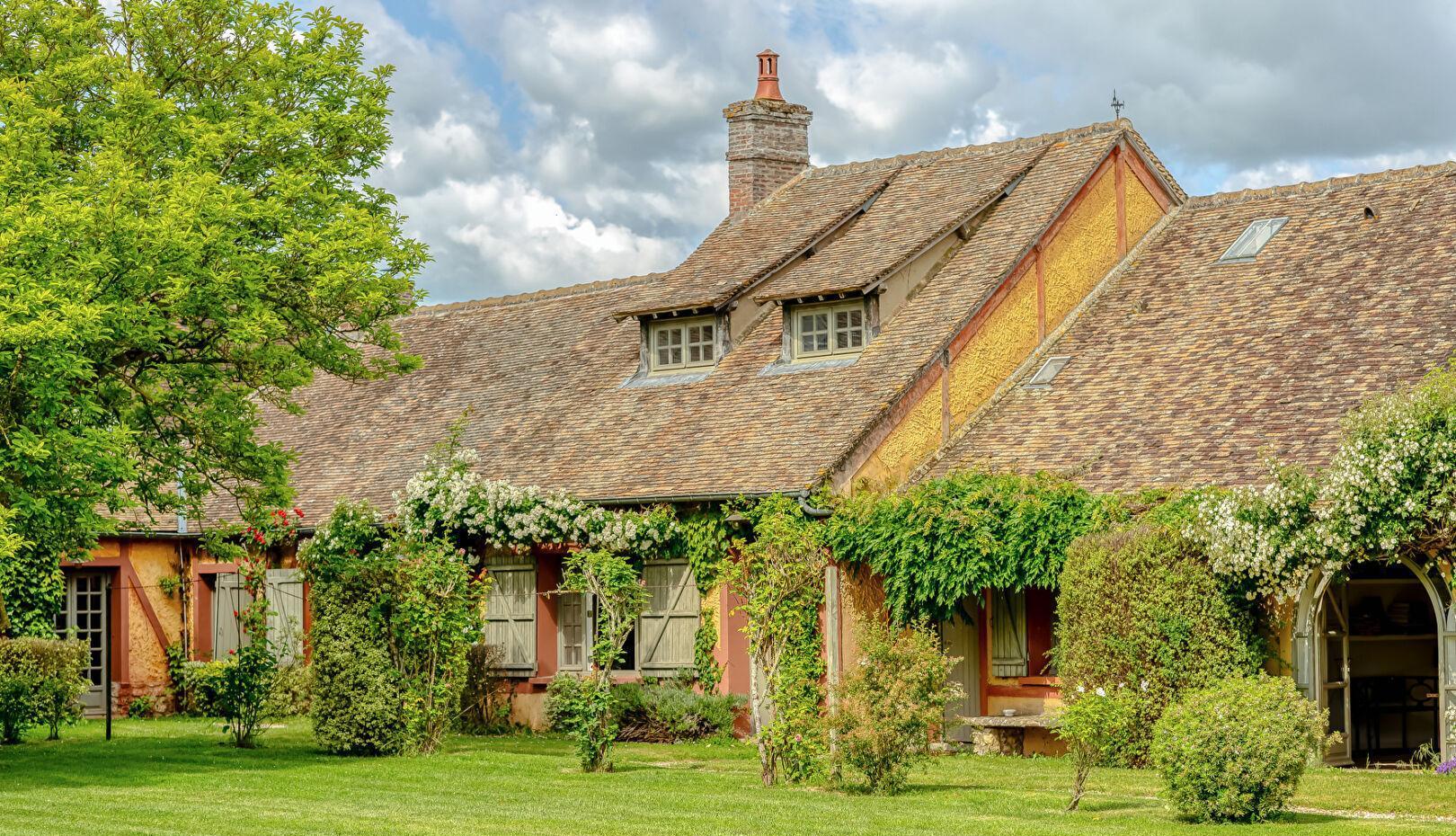 Maison de caractère en briques et colombages couverte de rosiers grimpants, dans la vallée de l'Eure