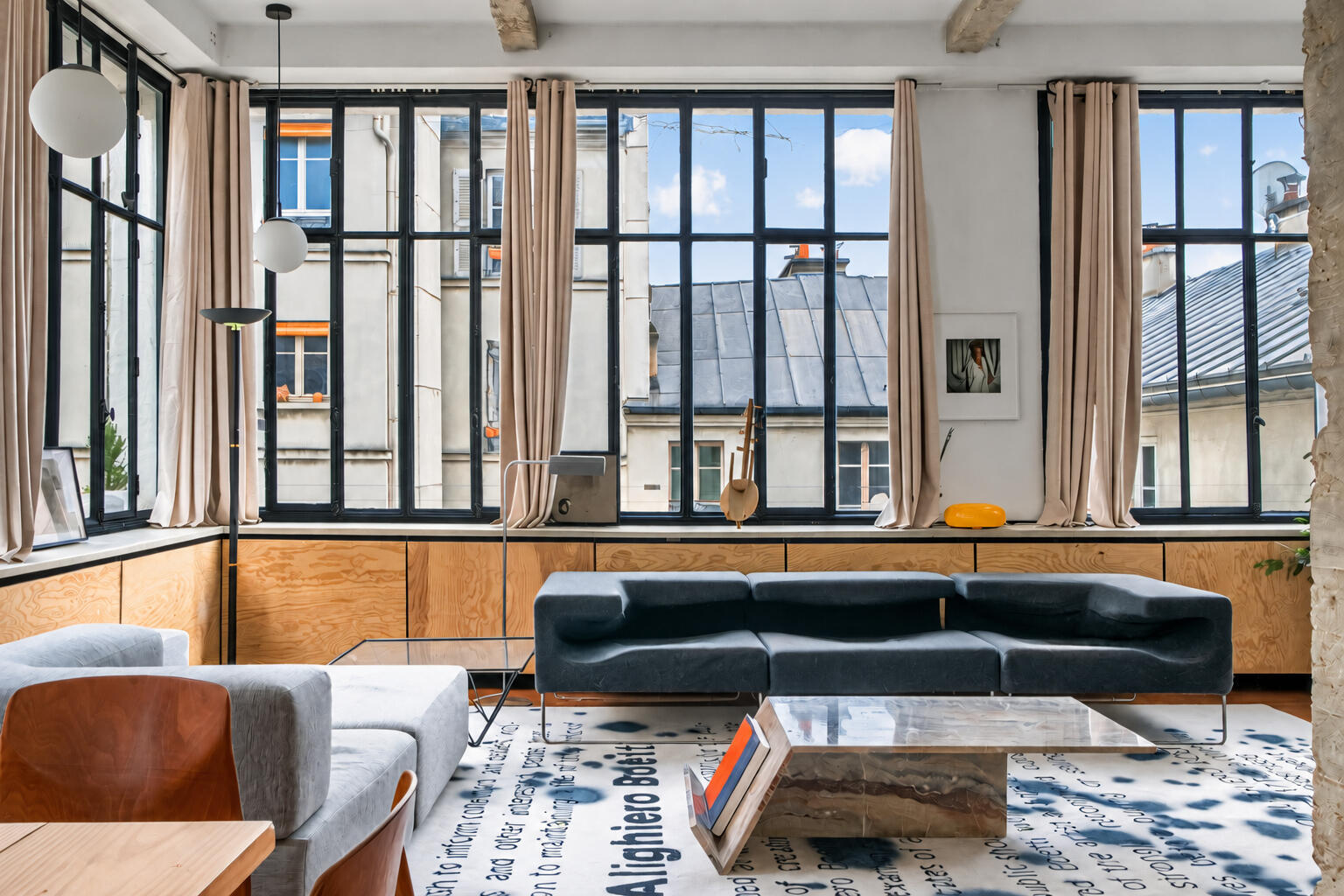 Loft aux grandes verrières d'atelier avec canapé en cuir noir et vue sur les toits