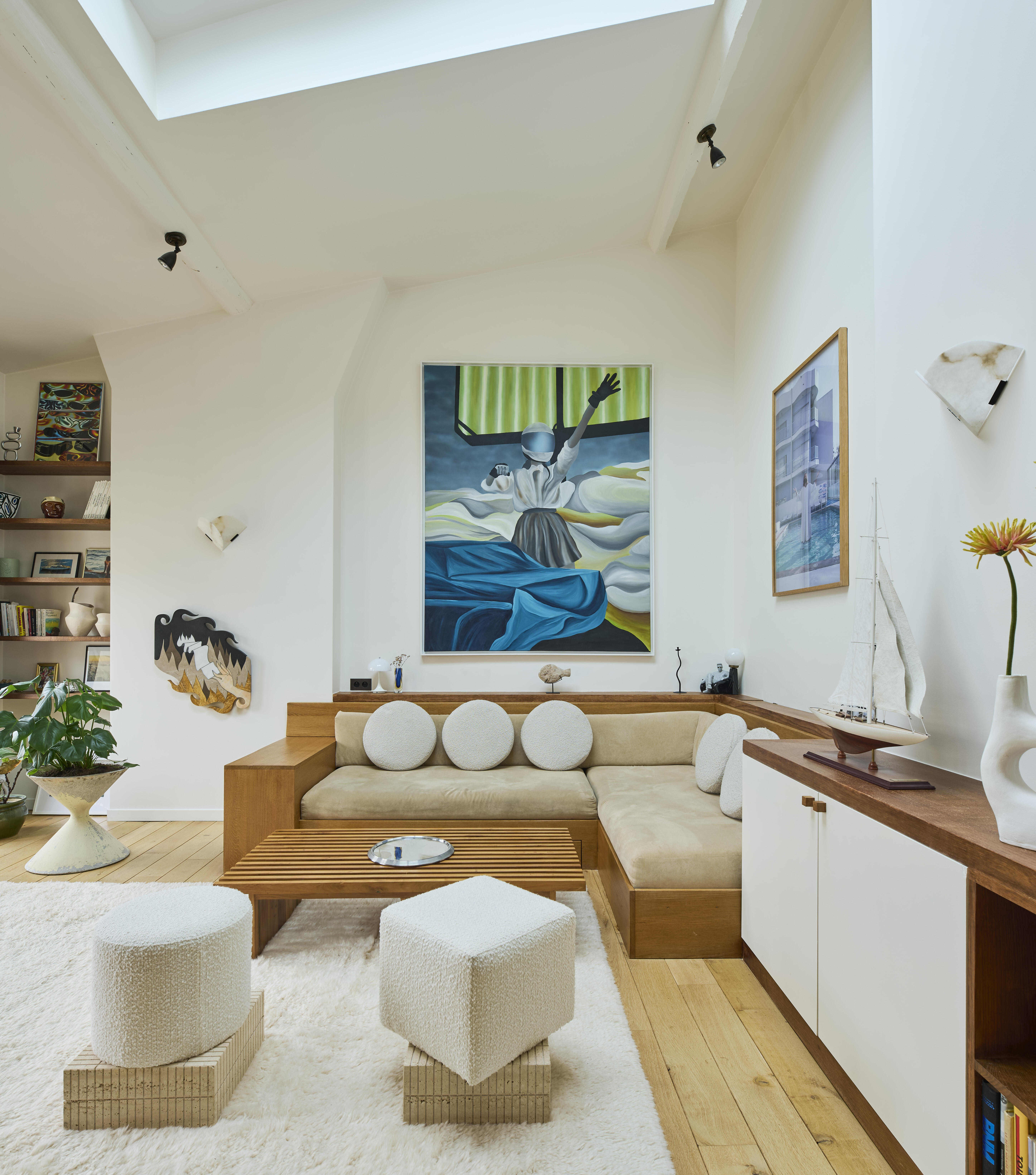 Salon mansardé baigné de lumière par des fenêtres de toit, avec canapé beige et rangements sur mesure