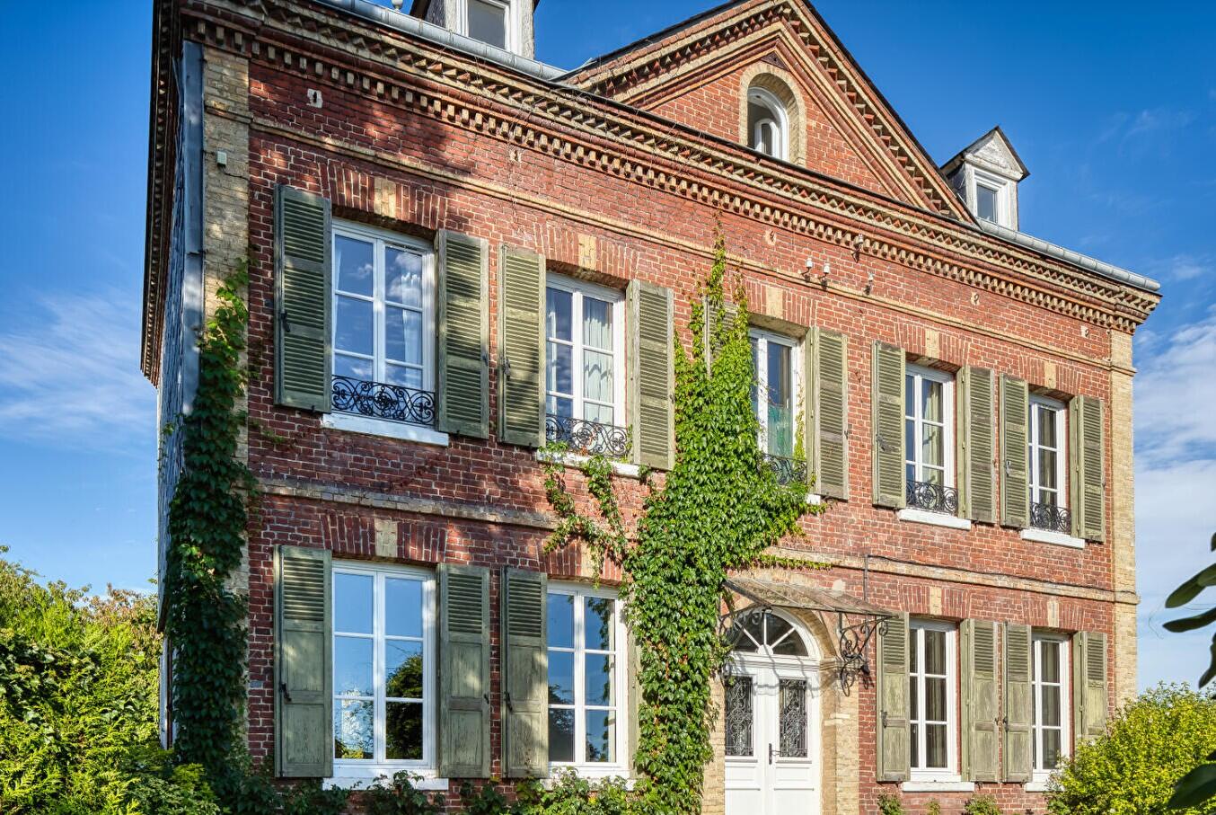 Façade d'une maison de maître en brique et pierre avec volets en bois, balcons en fer forgé et toit d'ardoise, dans l'Eure